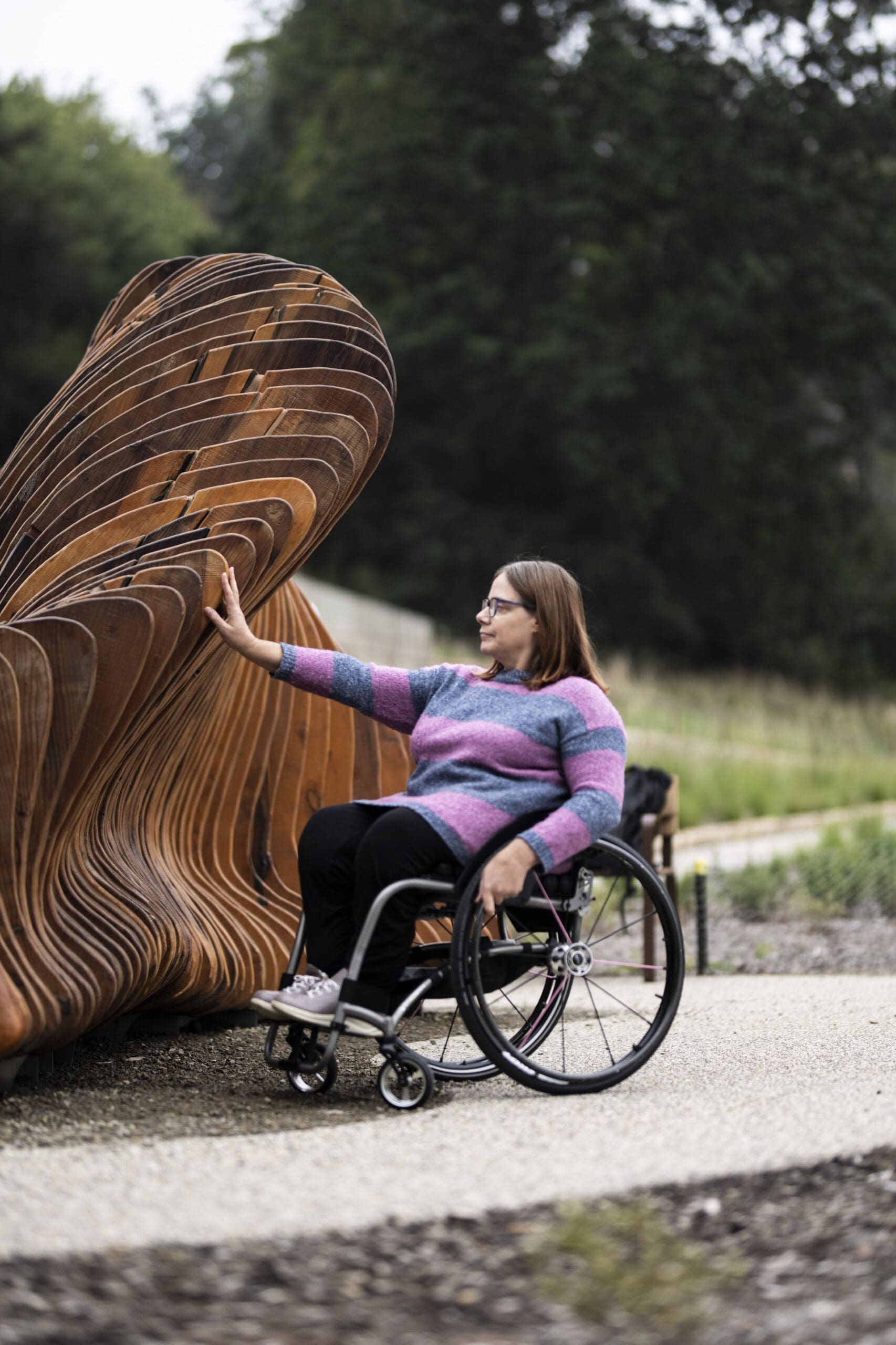 A woman in a wheelchair enjoys the accessible path to ngurrak barring artwork.